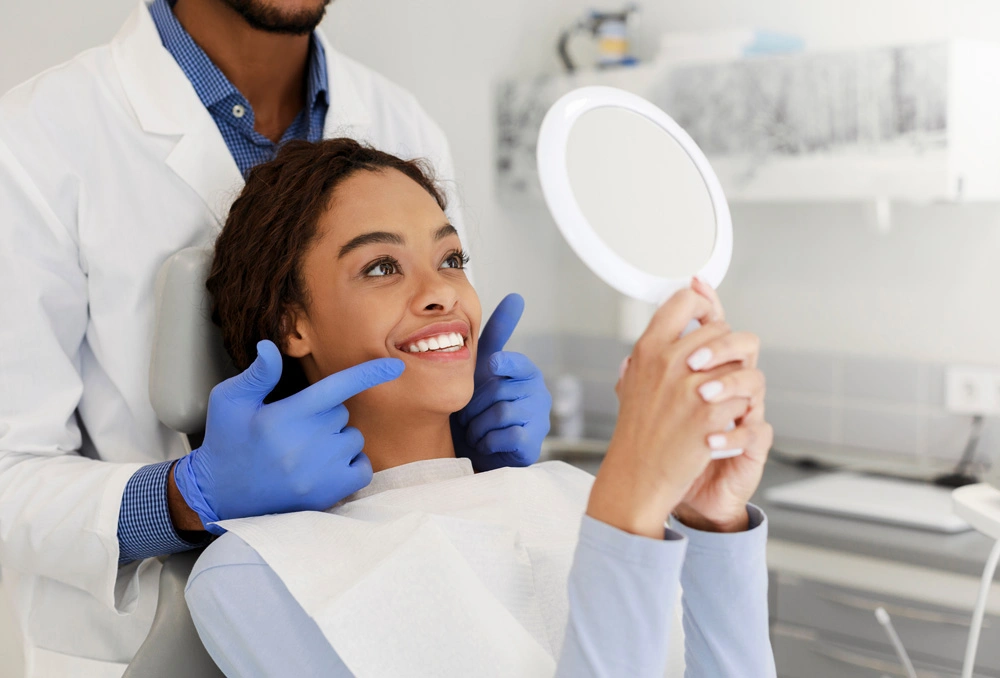 Attractive black lady checking her beautiful smile in mirror after treatment