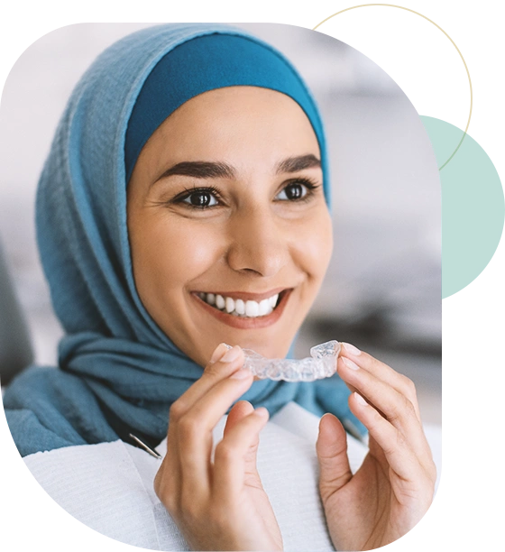 Smiling Muslim Woman In Hijab Holding Invisalign Or Invisible Braces While Sitting At Dentists Chair In Clinic